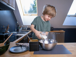 The boy prepares the dough from eggs, sugar, sour cream and flour by himself in the kitchen