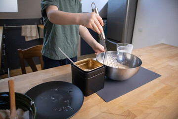 The boy prepares the dough from eggs, sugar, sour cream and flour by himself in the kitchen