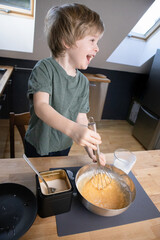 Fototapeta na wymiar The boy prepares the dough from eggs, sugar, sour cream and flour by himself in the kitchen