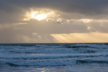 Foamy sea waves and sun peaking through the clouds at early evening