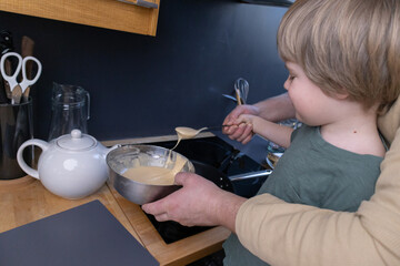 Father and son in the kitchen preparing batter for pancakes and cooking them.