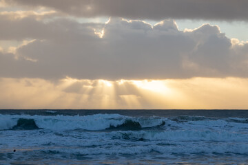 Rays of bright sun break through the clouds over the blue sea and the waves