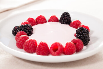 fresh raspberries and blackberries laid out on a white plate in circle with yogurt