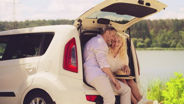 Happy middle-aged couple hugging and enjoying summer car picnic by the lake