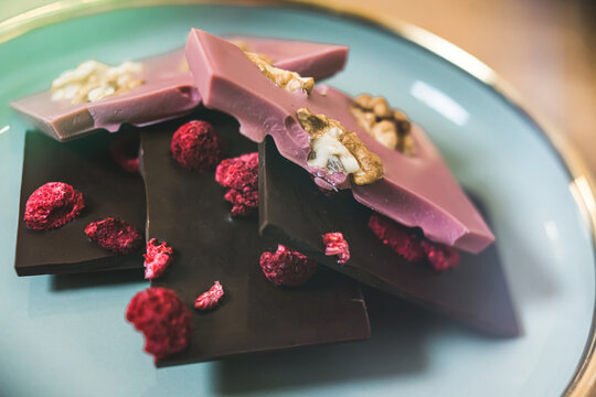 Broken bars of premium craft chocolate with dried raspberry and walnuts. High quality photo