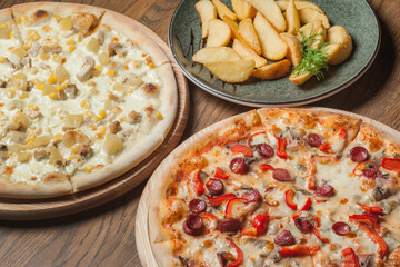 Two different pizzas on the boards and fried potatoes in a plate on the table