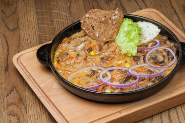 Baked meat with mushrooms, vegetables and greens in a pan on a board
