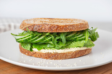 Sandwich with hummus, avocado, cucumber and herbs in a white plate