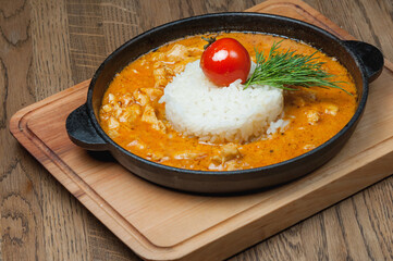 A dish of curry chicken with boiled rice, tomato and greens in a pan