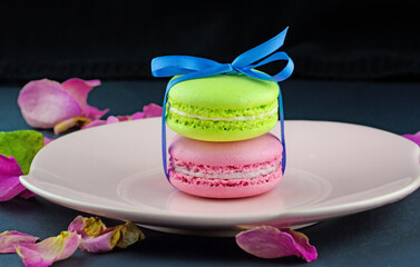 Colorful macaroons decorated blue ribbon with bow in pink plate with dried rose petals