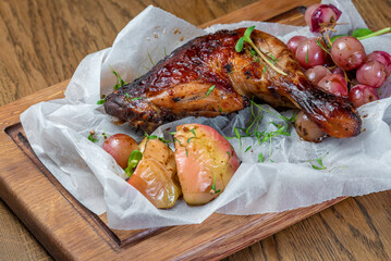 baked chicken thigh with vegetables and grapes in white paper on a board