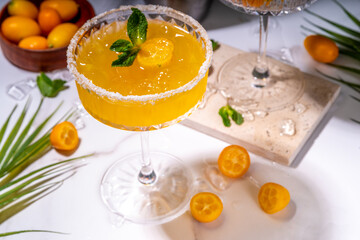 Sweet and salted Kumquat margarita cocktail garnished with kumquat slices  and mint, on marble and dark green tropical palm decorated background copy space