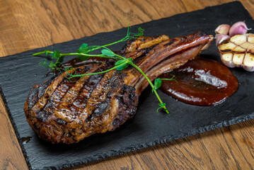 Grilled prime rib lies on a black board with sauce and a sprig of greens
