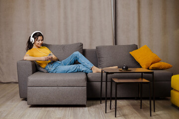 Happy indian or arabian girl resting on cozy sofa at home, listening to music