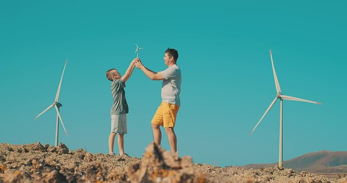 Happy father and son on looking at wind energy turbine sat wind farm site, alternative energy, wind farm and happy time with your family.