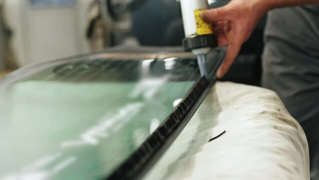 Skilled mechanic carefully adding glue to the windscreen of the car for replacement. High-quality 4k footage