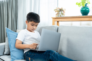 Asian boy sitting open notebook, studying online morning, sitting on living room sofa house, looks determined to study, When class was finished, they sat down to do homework that teacher ordered.