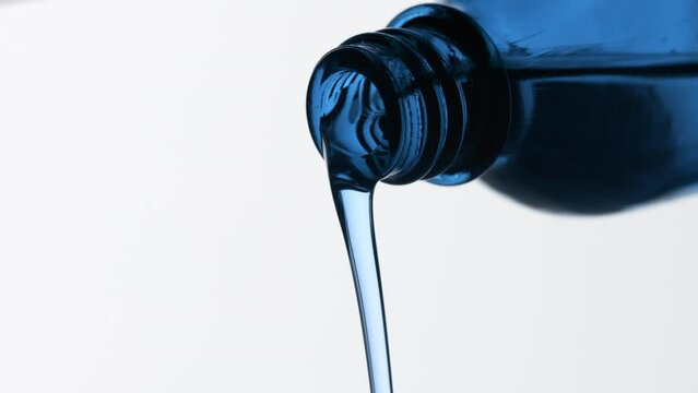 Macro shot of blue tansy oil is being poured from blue reagent bottle on grey background | Abstract face care cosmetics ingredients formulating concept