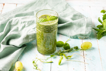 Healthy smoothie of sprouted wheat, peas and other microgreens in a glass glass, wooden background.