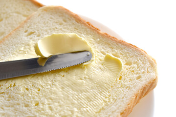 Butter on bread on a white plate.  A knife spreading butter on bread. 