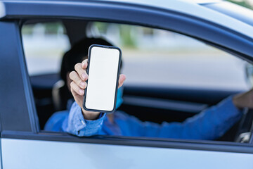Male hand holding a smartphone with a white mockup on the screen. car steering wheel background Young man showing phone screen sitting in the driver's seat The app driver calls the user.