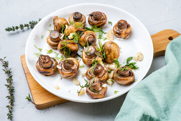 Champignons roasted with herbs and garlic and served in a white plate on a board, gray background.