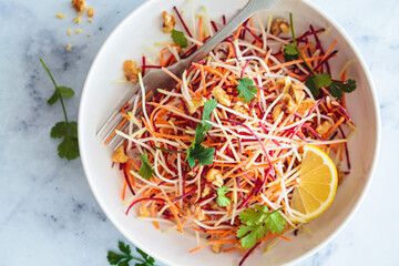 Spring carrots, beets, cabbage salad with nuts and herbs in white bowl.