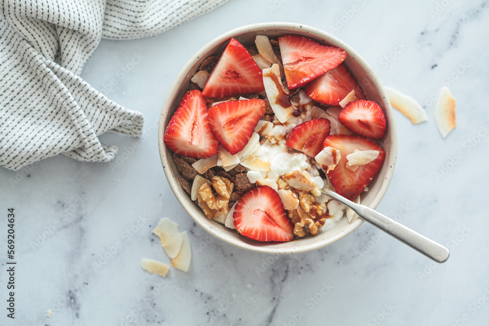 Wall mural Cottage cheese bowl with strawberries, cereal flakes, coconut, nuts and syrup, marble background.