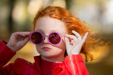 Portrait of a stylish red-haired girl in purple round sunglasses.