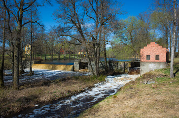 Fototapeta na wymiar Small hydroelectric dam on Svartan river in Skerike with old red brick Turbine house, Spring nature in Sweden