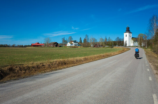 Swedish countryside road to the white building of the Karbenning church along a green field on a warm spring sunny day, cycling holidays in Scandinavia
