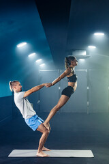 Young fit woman and man in sportswear doing acrobatics yoga at gym.