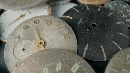 Old worn clock dials. Aged scratched round watch faces with hands and numbers. Pile of metal broken and disassembled watch dials. Vintage timepiece in the workshop, repair. Close up.