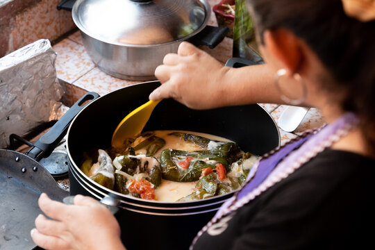 unrecognizable woman mixing with a wooden spoon homemade pepper stuffed with cheese and cream sauce, latin food