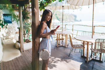 Happy young lady messaging on smartphone in outdoor cafe at seaside