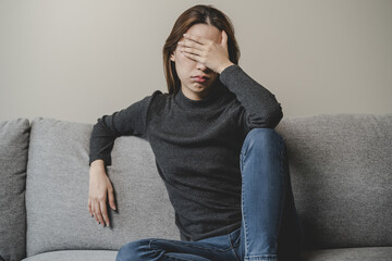 Unhappy anxiety young Asian woman covering her face with pillow on the cough in the living room at home.