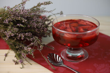 sweet delicious fragrant fruit jelly dessert with fresh strawberries in a transparent glass next to a vase with flowers. for labels, menus, splash screens, flyers, banners, and more