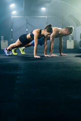 Fototapeta premium Muscular man and woman in sportswear doing push up in gym.