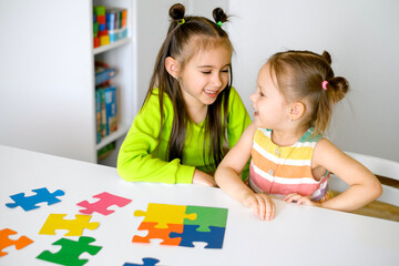 Children collect puzzles together at the desk in the children's room.Development of logic and thinking of preschool children. Acquisition of skills