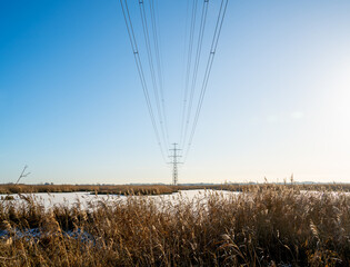 Obraz premium Winter landscape with frozen lake and row of power pylons 