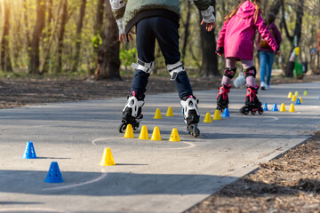 Group of little children enjoy having fun learning inline roller skate slalom with plastic cones on...