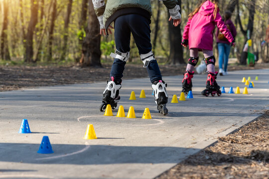Group of little children enjoy having fun learning inline roller skate slalom with plastic cones on road in city park outdoors on sunny spring day. Healthy kid outside sport exercise activities