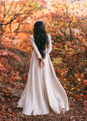 Mystery art portrait fantasy woman queen walking in gothic autumn forest, white vintage style dress. Girl princess long wavy brunette hair, medieval sexy lady. Red orange yellow color dark tree park