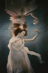 Portrait of a girl in a dress floating underwater as if she were in a weightlessness
