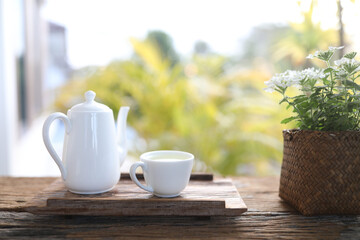 white tea cup and tall tea pot and Verbena plant pot wooden table balcony