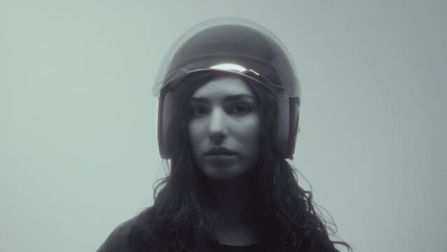 A young attractive girl puts on a helmet. A beautiful woman in a leather jacket puts on a plastic protective helmet for a motorcycle or scooter. Urban lifestyle. Independent and strong girl, feminism