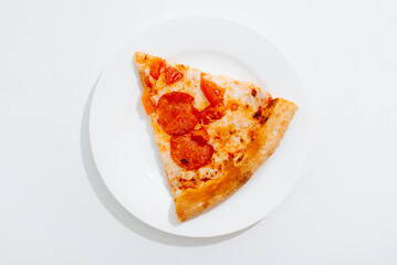 Pepperoni pizza slice with mozzarella, tomato, sauce on white plate on table, top view