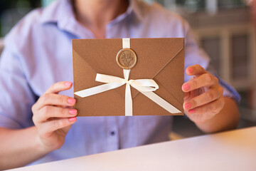 Closeup photography of woman,holding a bronze invitation envelope with wax seal and satin ribbon.