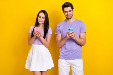 Photo of two positive bloggers hold use smart phone write typing blog post isolated on yellow color background