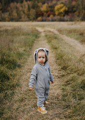 Sad little child in a grey bunny costume standing in an open field.